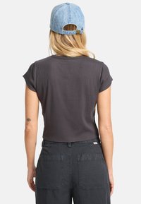 Camisa de manga corta de color gris oscuro con cuello redondeado, combinada con pantalones oscuros de cintura alta y una gorra de denim azul claro.