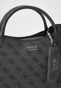 Borsa nera con superficie testurizzata, caratterizzata da un motivo a diamante, doppio manico e logo dorato. Include un'etichetta in pelle con dettagli.
