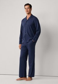 Conjunto de pijama azul marino con un patrón geométrico, camiseta con botones de mangas largas y pantalones a juego, fabricado en una textura suave, con un corte relax.