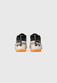 Pair of black and beige Salomon hiking shoes with orange soles, viewed from the back on a plain light gray background.