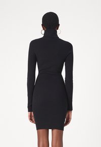Robe noire en maille côtelée avec manches longues et col montant, dotée d'une coupe ajustée s'étendant au-dessus du genou.