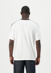 Witte t-shirt met korte mouwen, een zwarte ronde hals en schouderaccenten. Gladde textuur en een losse pasvorm, gezien vanaf de achterkant.