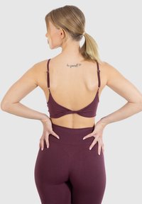 Bordeaux sportbh met een gedraaide achterkant, verstelbare bandjes en een aangesloten high-waisted legging, gemaakt van een zachte stof.