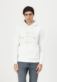 Weißer Hoodie mit einer Fronttasche, Kapuze mit Kordelzug und bedrucktem Textdesign. Trägt man mit blauen Jeans, glatte Stoffstruktur.