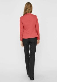 Korallinvärinen bleiseri, jossa on jämäkkä malli, kaulus, ja kaksi nappia, yhdistetty mustiin housuihin. Kangas näyttää sileältä ja hyvin viimeistellyltä.