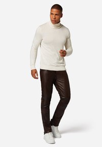 Witte coltrui gecombineerd met donkerbruine leren broeken en witte sneakers. De trui heeft een slim fit ontwerp en ribgebreide manchetten.