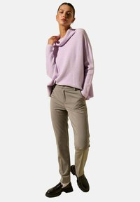 Pull en lilas à côtes avec un col cheminée, assorti à un pantalon beigne fuselé et des mocassins noirs, présentant une texture lisse et des détails subtils.