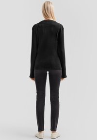 Zwart geribd langarmshirt met een ronde hals, gecombineerd met donkere slim-fit jeans en lichtgekleurde instapschoenen.