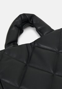 Czarna pikowana torba na ramię z gładkiej skóry, z masywnym, pętlowym uchwytem i pikowaniem w kształcie diamentów, nadającym teksturę.