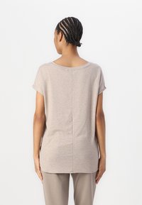 Ljus beige t-shirt med kort ärm och rundad halsringning, med en central söm och en avslappnad passform. Tyget verkar mjukt och något texturerat.