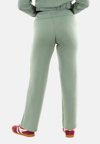 Lichtgroene joggingbroek met een gladde textuur, elastische tailleband, rechte pijpen en zijaccenten, gecombineerd met rode en witte sneakers.