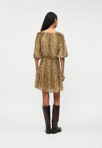 Kratké rukávy, šaty s leopardím potiskem v barvách tan a černé, s nařaseným pasem a rozšířenou sukní. V kombinaci s hnědými vysokými kozačkami.