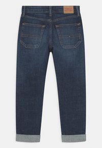 Tmavě modré džínové kalhoty s rovnými nohavicemi, ohrnutými manžetami, zadními kapsami a béžovou koženou nášivkou na pásku.