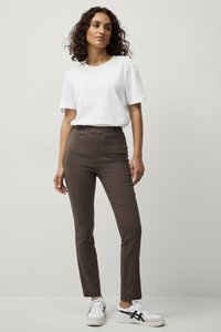 T-shirt en coton blanc associé à un pantalon ajusté marron. Modèle portant des baskets blanches avec des accents noirs. Design simple, texture lisse et sans motifs.