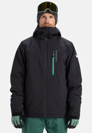 Black ski jacket with a high collar, blue-green zip pocket, adjustable cuffs, and seamless design; gloves in green and black.