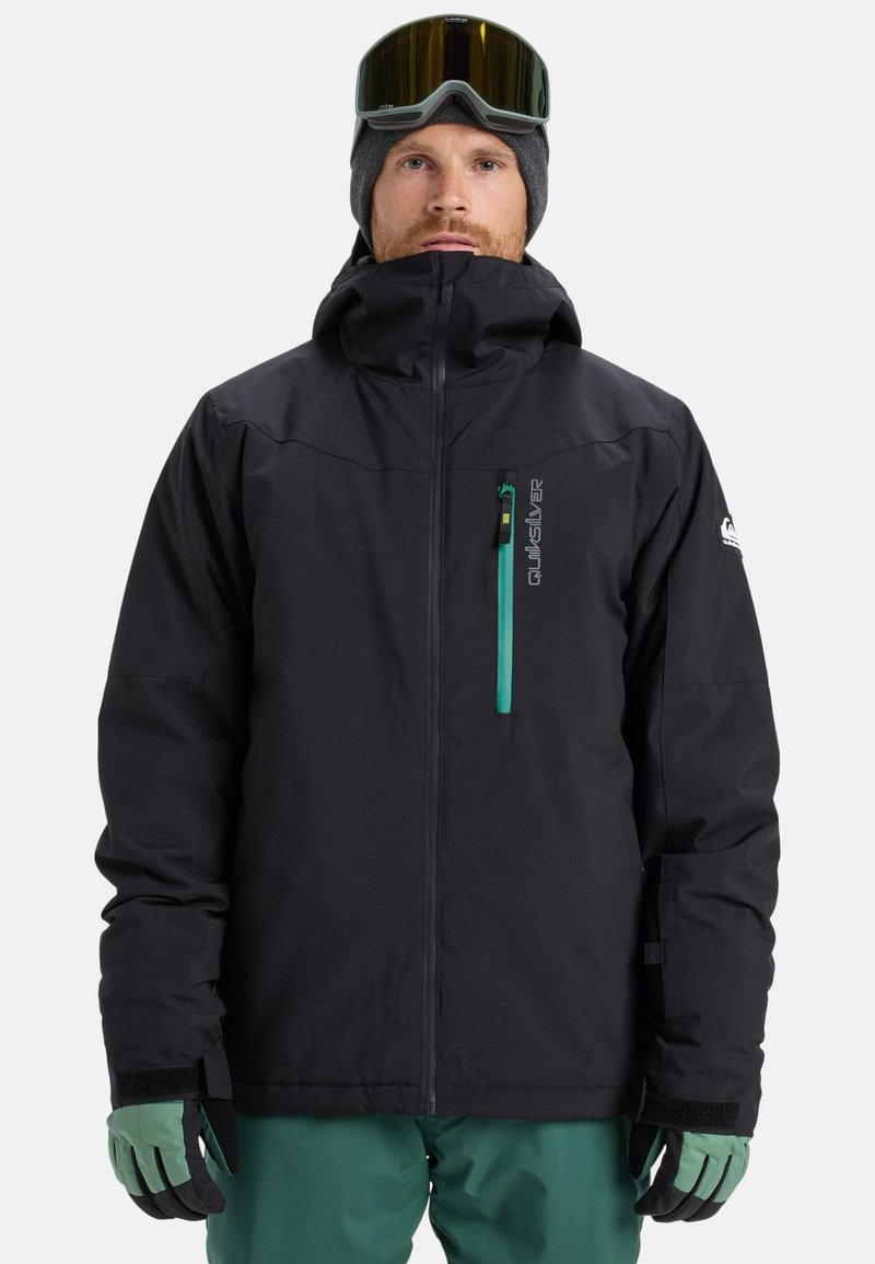 Schwarze Skijacke mit hohem Kragen, blau-grüner Reißverschlusstasche, verstellbaren Bündchen und nahtlosem Design; Handschuhe in Grün und Schwarz.