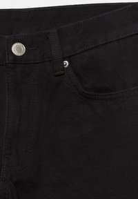 Gros plan sur la ceinture d'un jean en denim noir avec un bouton en métal, une boucle de ceinture et le bord d'une poche avant avec des coutures visibles.
