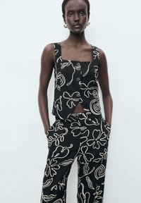 Ensemble noir composé de deux pièces en tissu texturé, arborant des motifs floraux abstraits blancs, un haut à encolure carrée avec des boutons et un pantalon à jambes larges.