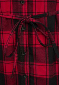 Camicia a quadri rossi e neri con apertura a bottoni, bottoni neri e cintura da annodare in vita; realizzata in tessuto texturizzato.