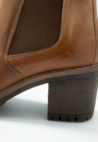 Braune Leder-Ankle-Boots mit strukturiertem Finish und elastischem Seitenpaneel, ausgestattet mit einem klobigen Holzabsatz und einer kontrastierenden Zuglasche.