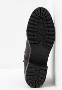 Semelle d'une bottine noire montrant un motif de crampons profonds, taille 37, avec le nom de la marque "Anna Field" sur la zone du talon.