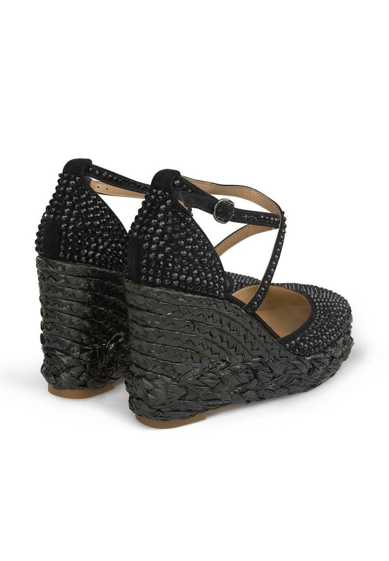 Zapatos de cuña negros con una base tejida texturizada, parte superior con tachuelas y una correa para el tobillo con un broche seguro. Diseño clásico de punta redonda.