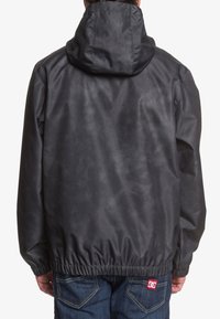 Black, lightweight jacket with a hood, elastic waistband, and smooth texture. No visible graphics; back view shows a simple design.