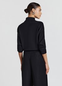 Pull-over noir avec un col montant, des manches trois-quarts et un ourlet côtelé. Associé à un pantalon noir assorti, mettant en valeur la texture lisse du tissu.