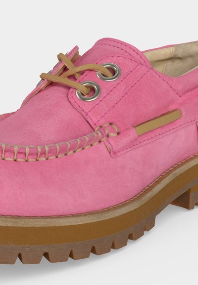Κοντινή λήψη ενός ροζ καστόρινού παπουτσιού τύπου boat με μπεζ δερμάτινα κορδόνια, μπεζ ραφές, μεταλλικές οπές και παχύ καφέ καουτσούκ πάτο.