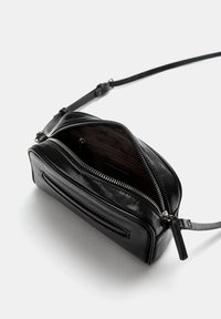 Svart läder crossbody-väska med dragkedjestängning, slät textur, liten framficka och justerbar rem. Inredning i brunt.