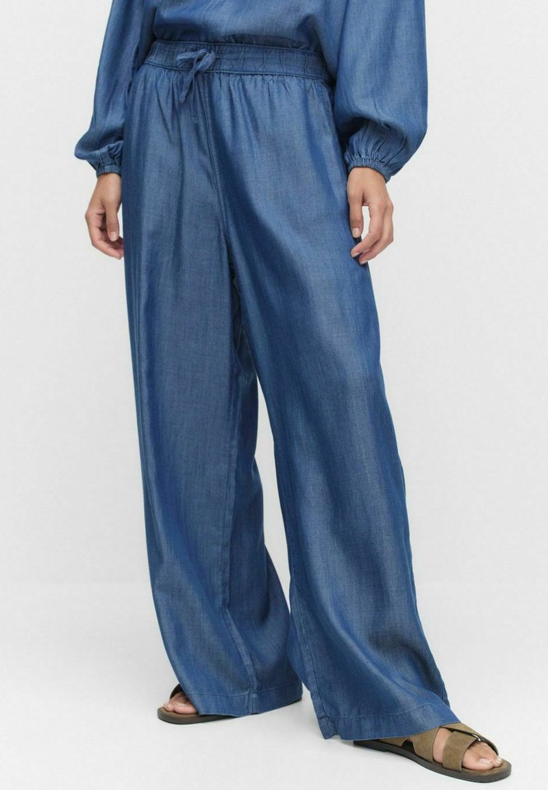 Denim vida byxor med elastisk midja och dragsko, med en slät textur och en djup blå färg, kombinerade med platta sandaler.