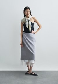 Gaiši pelēka zīmuļu svārki ar mežģīņu apakšmalu, kopā ar melnu strapless topu un rakstainu šalli, valkāti ar melnām plakanām kurpēm.