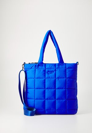 Blå, quiltet tote bag med rektangulær form, polstret tekstur, doble håndtak og en avtakbar stropp. Har glidelås og logo-detalj.