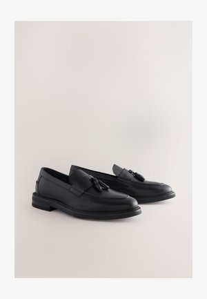 Pantofi loafer din piele neagră, cu finisaj neted, având un accesoriu decorativ cu ciucure și o talpă robustă din cauciuc. Design clasic slip-on.