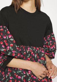 Czarna bluzka z krótkimi bufkami, w kwiatowy druk wiśni na czarnym tle, z marszczoną talią i miękką bawełnianą teksturą.
