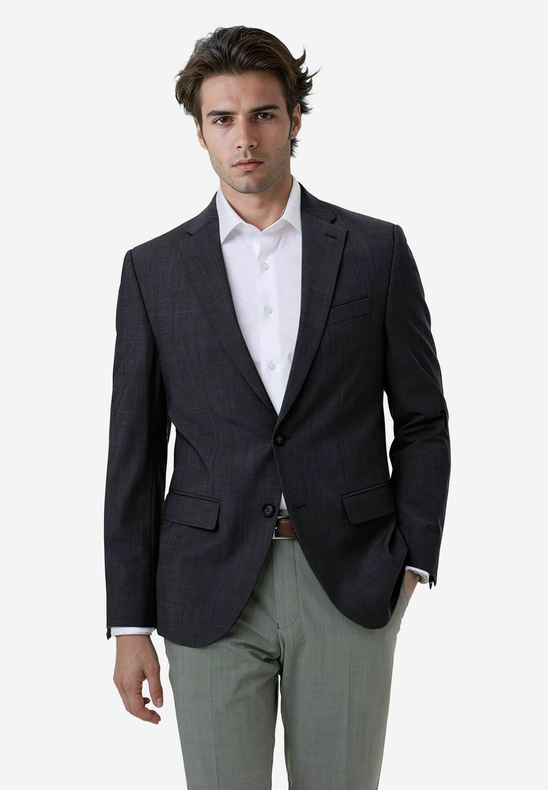 Dunkelkarierter Blazer aus glattem Stoff, mit zwei vorderen Taschen, mit geschlitzten Revers und einem Ein-Knopf-Verschluss, kombiniert mit hellen Hosen.