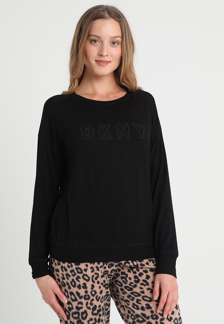 Czarny sweter z długim rękawem i okrągłym dekoltem, z podniesionym logo "DKNY" z przodu; zestawiony z brązowymi spodniami w lamparty.