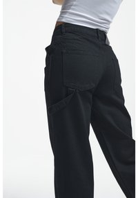 Pantaloni cargo neri con vestibilità rilassata, dotati di molteplici tasche e una texture morbida. Il tessuto appare resistente con dettagli di cucitura discreti.