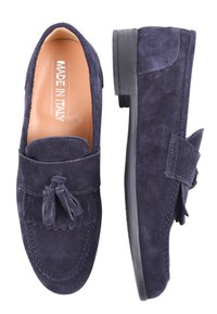 Mocassini in suede blu navy con un accento a nappina, cuciture da mocassino e una suola piatta in gomma nera. L'interno presenta un'etichetta "MADE IN ITALY".