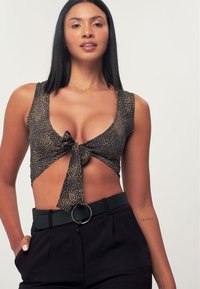 Top corto con stampa leopardata, scollatura a V profonda e nodo frontale. Abbinato a pantaloni neri a vita alta e una cintura con fibbia tondeggiante.