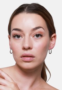 Orecchini a cerchio in argento a forma di U, dalla texture liscia e dalla finitura lucida, indossati da una modella con trucco neutro e pelle chiara.