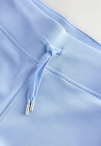 Ljusblått tyg med en mjuk yta, utrustat med en dragsko med silverändar och platta sömmar. Diskret och enhetlig design.