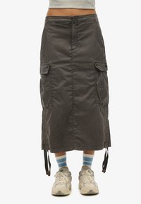 Cargoskirt gemaakt van donkergrijs stoffen, heeft twee zijzakken, een knoopsluiting aan de voorkant en verstelbare koordjes aan de zoom. Gecombineerd met sneakers.