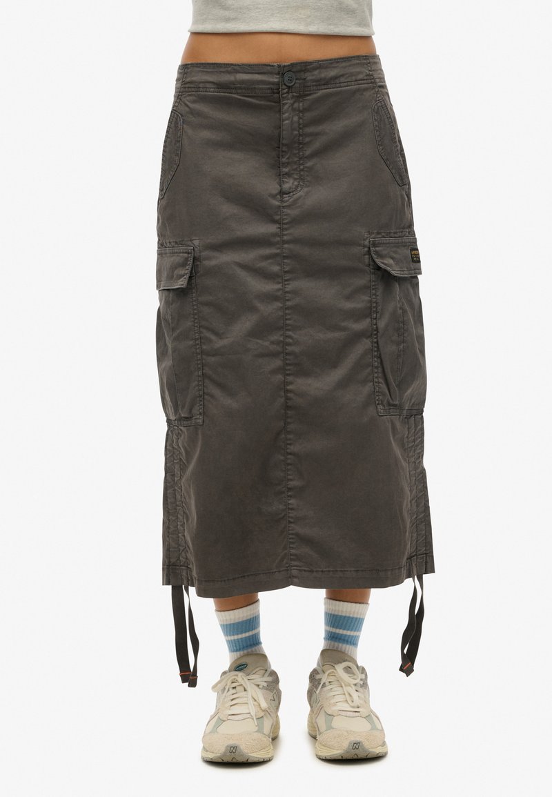 Cargoskirt gemaakt van donkergrijs stoffen, heeft twee zijzakken, een knoopsluiting aan de voorkant en verstelbare koordjes aan de zoom. Gecombineerd met sneakers.