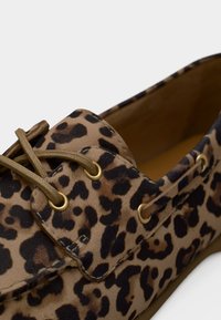Παπούτσι με λεοπάρ μοτίβο σε αποχρώσεις ταμπά και σκούρου καφέ υφάσματος, με χρυσά οπές και μπεζ κορδόνια. Διαθέτει στρογγυλεμένη μύτη και ομαλή υφή.