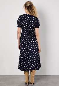 Navyblaues Kleid mit weißen Polka-Dots, kurzen Puffärmeln, taillierter Taille und knöchellangem Rock. Geschmeidige Textur und kreisförmiges Muster im gesamten Kleid.