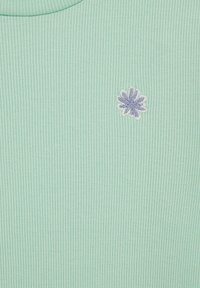 Menta zöld bordázott anyag, kis hímzett virággal, amely lágy lila és fehér színekben jelenik meg. Egyszerű, kerek nyakkivágás, látható záródás nélkül.