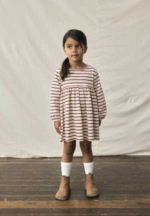 Robe à manches longues rayée en crème et bordeaux avec une taille froncée. Associée à des bottes chelsea beiges et des chaussettes blanches montantes.