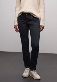 Mörkblå denimjeans med smal passform, med fem fickor, silverfärgade detaljer och subtil textur, kombinerade med en ljus tröja och sneakers.