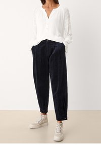 Camicia bianca, con bottoni e spalle arricciate, abbinata a pantaloni in velluto a coste blu scuro. Le sneakers presentano una suola testurizzata e un design con lacci.